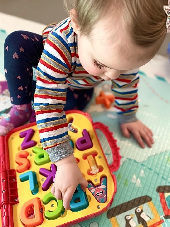 A baby crawling toward an adult's hand offering a toy during a session