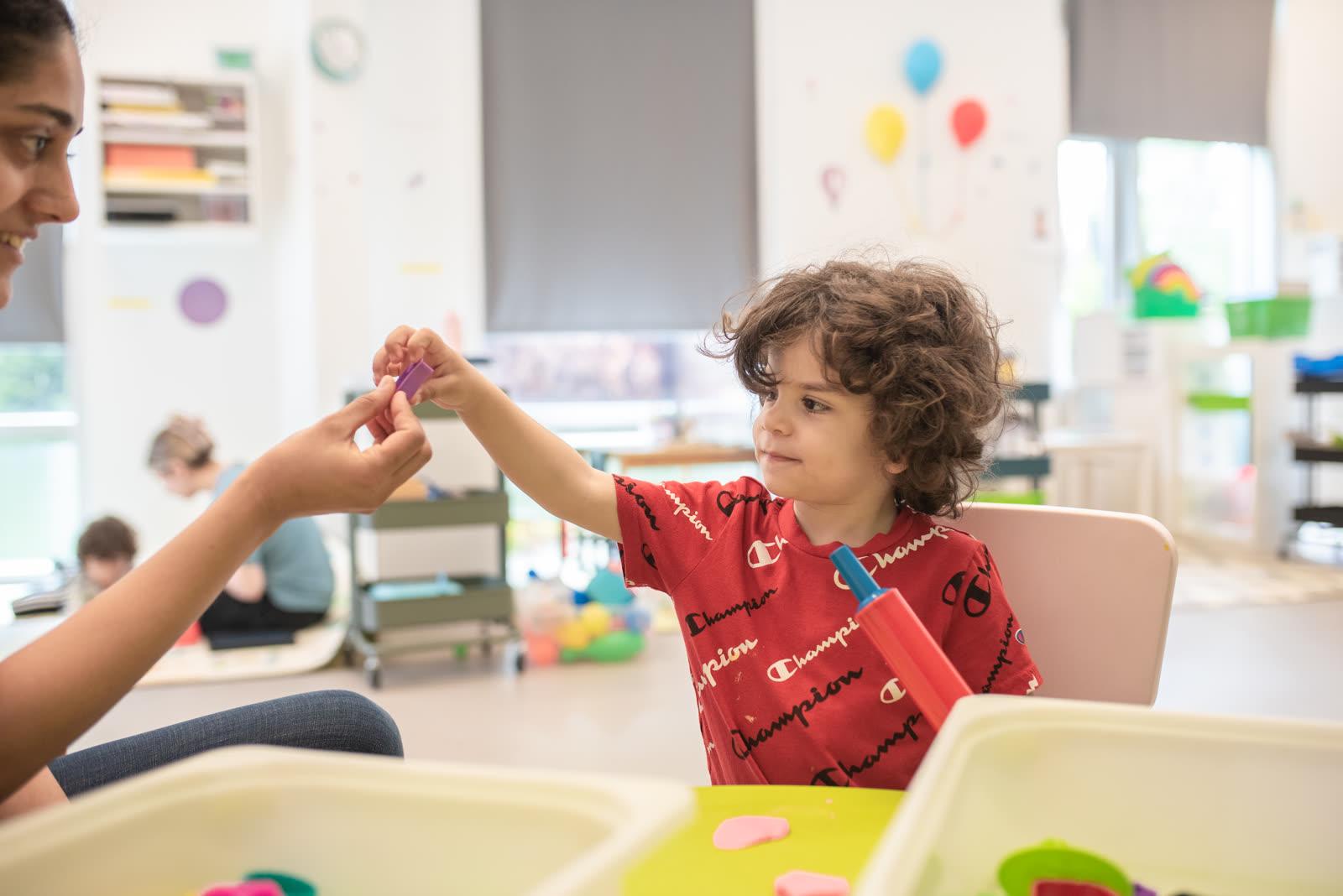 A clinician and a young child exchanging a building block at a table